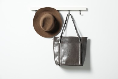 Photo of Brown hat and bag hanging on hook rack on white wall