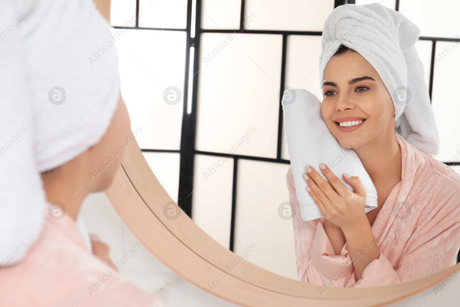 Photo of Young woman wiping face with towel near mirror in bathroom