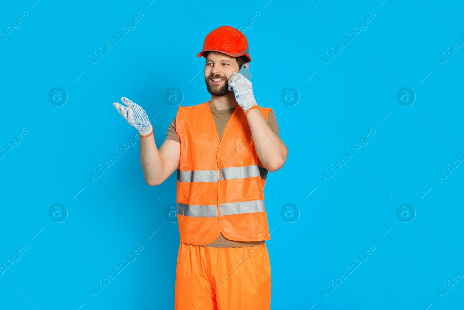 Photo of Man in reflective uniform talking on smartphone against light blue background