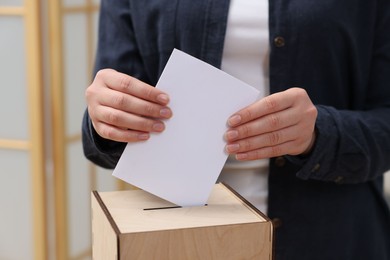 Photo of Woman putting her vote into ballot box on blurred background, closeup