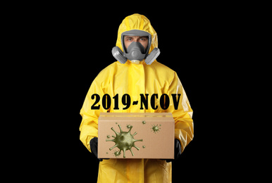 Man wearing chemical protective suit with cardboard box on black background. Coronavirus outbreak