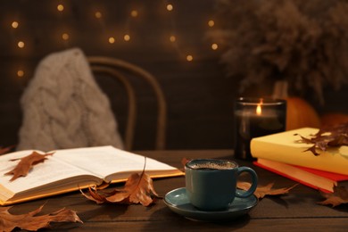Cup of aromatic coffee, books and autumn leaves on wooden table indoors. Space for text