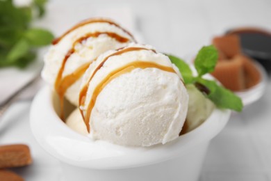 Photo of Scoops of tasty ice cream with mint leaves and caramel sauce on blurred background, closeup