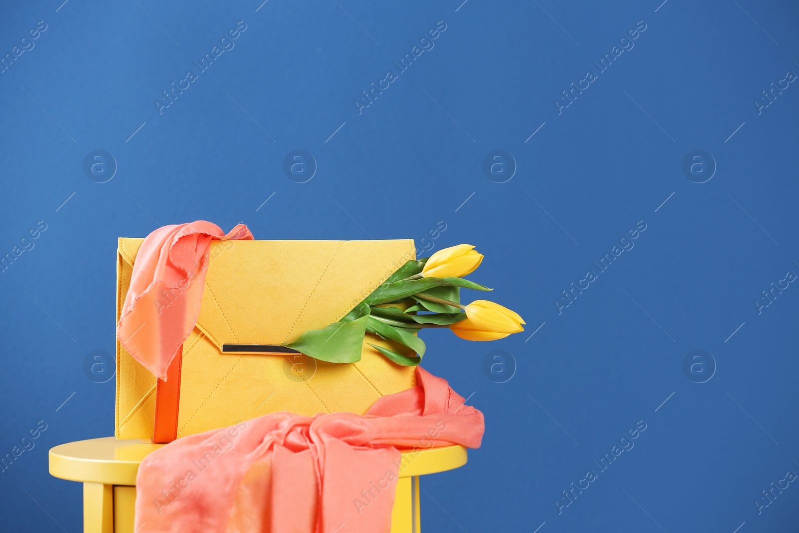 Photo of Elegant clutch with spring flowers and scarf on table against blue background. Space for text