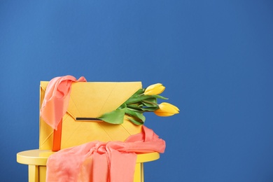 Photo of Elegant clutch with spring flowers and scarf on table against blue background. Space for text