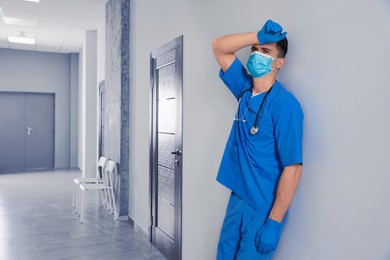 Exhausted doctor near grey wall in hospital, space for text