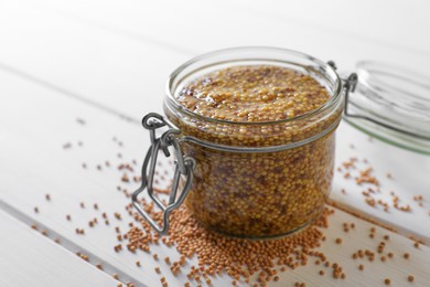 Photo of Jar of whole grain mustard on white wooden table, closeup