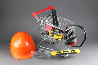 Photo of Small shopping cart with set of construction tools. protective glasses and hard hat on grey background
