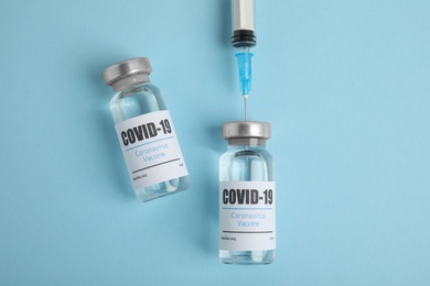 Photo of Filling syringe with coronavirus vaccine on light blue  background, flat lay