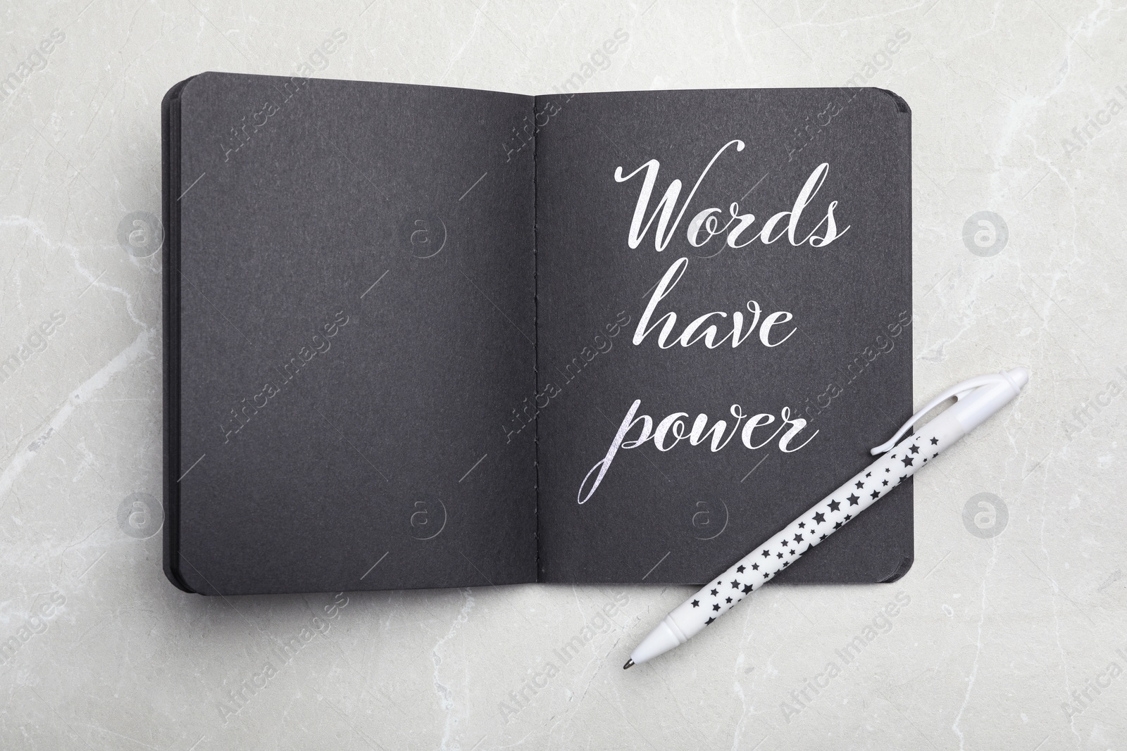 Image of Notebook with black pages and phrase Words Have Power on light grey marble table, top view