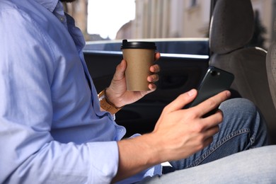 Photo of Coffee to go. Man with paper cup of drink and smartphone in car, closeup