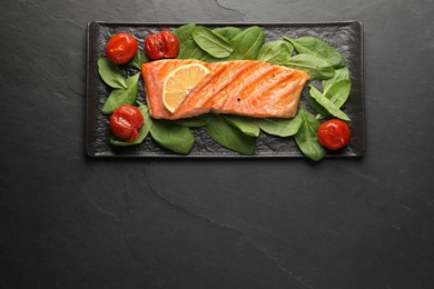 Photo of Tasty grilled salmon with tomatoes, spinach and lemon on black table, top view. Space for text