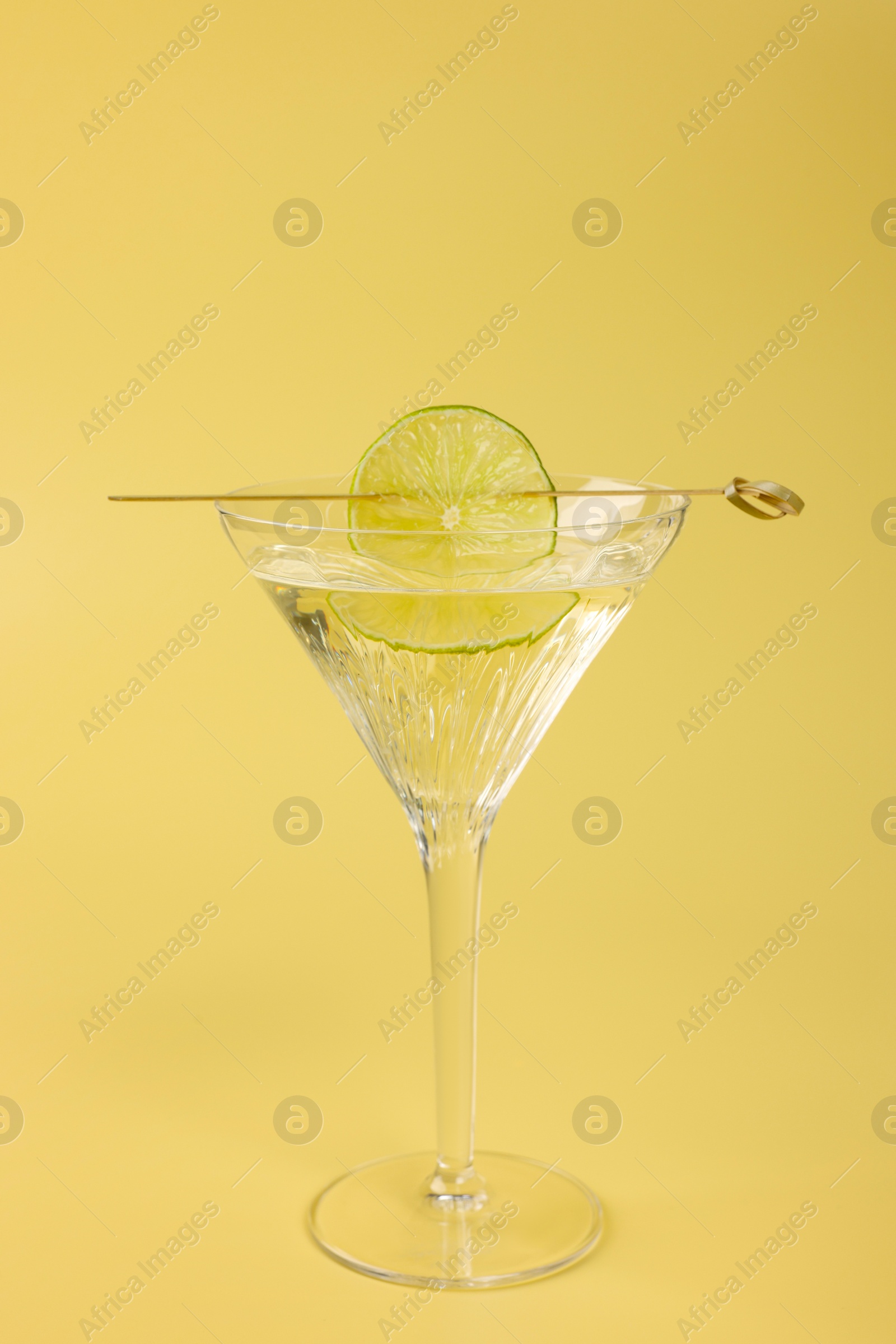 Photo of Martini cocktail with lime slice on yellow background