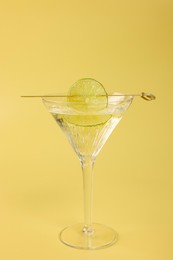 Martini cocktail with lime slice on yellow background