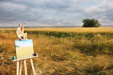 Photo of Wooden easel with beautiful picture and painting equipment in field. Space for text