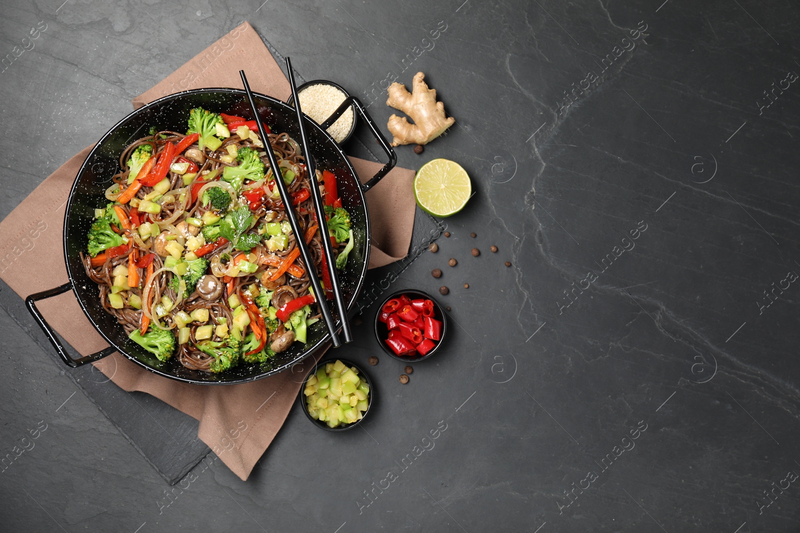 Photo of Wok with noodles, mushrooms, vegetables and other products on black table, flat lay. Space for text