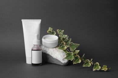 Cosmetic products, stone and ivy leaves on dark grey background