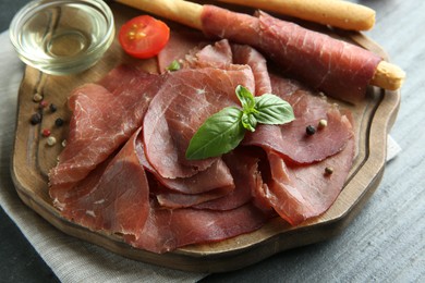 Photo of Delicious bresaola and basil leaves on grey textured table, closeup