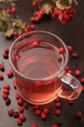 Cup with hawthorn tea and berries on wooden table, closeup