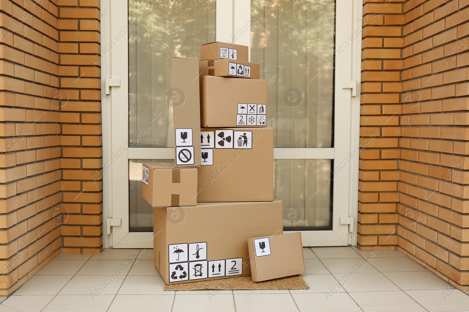 Photo of Cardboard boxes with different packaging symbols on door mat near entrance. Parcel delivery