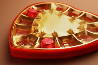 Photo of Partially empty heart shaped box of chocolate candies on brown background, closeup