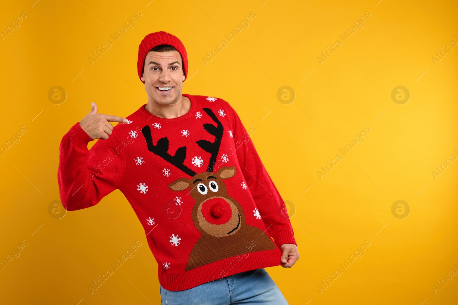 Photo of Happy man in hat showing his Christmas sweater on yellow background