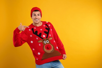 Photo of Happy man in hat showing his Christmas sweater on yellow background
