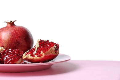 Plate with ripe pomegranates on table against white background, space for text