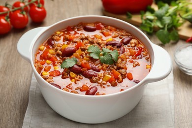 Photo of Bowl with tasty chili con carne on wooden table, closeup