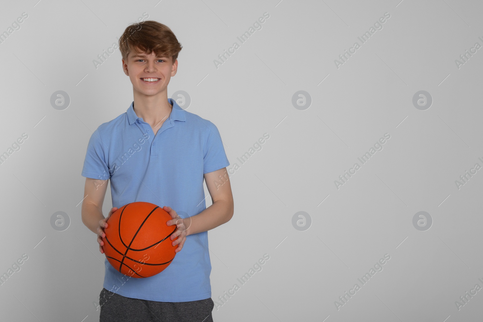 Photo of Teenage boy with basketball ball on light grey background. Space for text