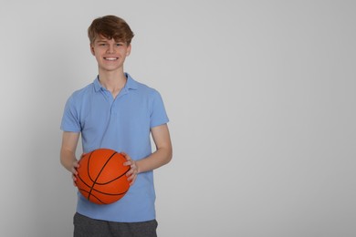 Teenage boy with basketball ball on light grey background. Space for text