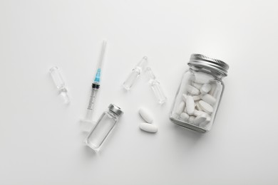 Photo of Glass ampoules with liquid, pills and syringe on white background, flat lay