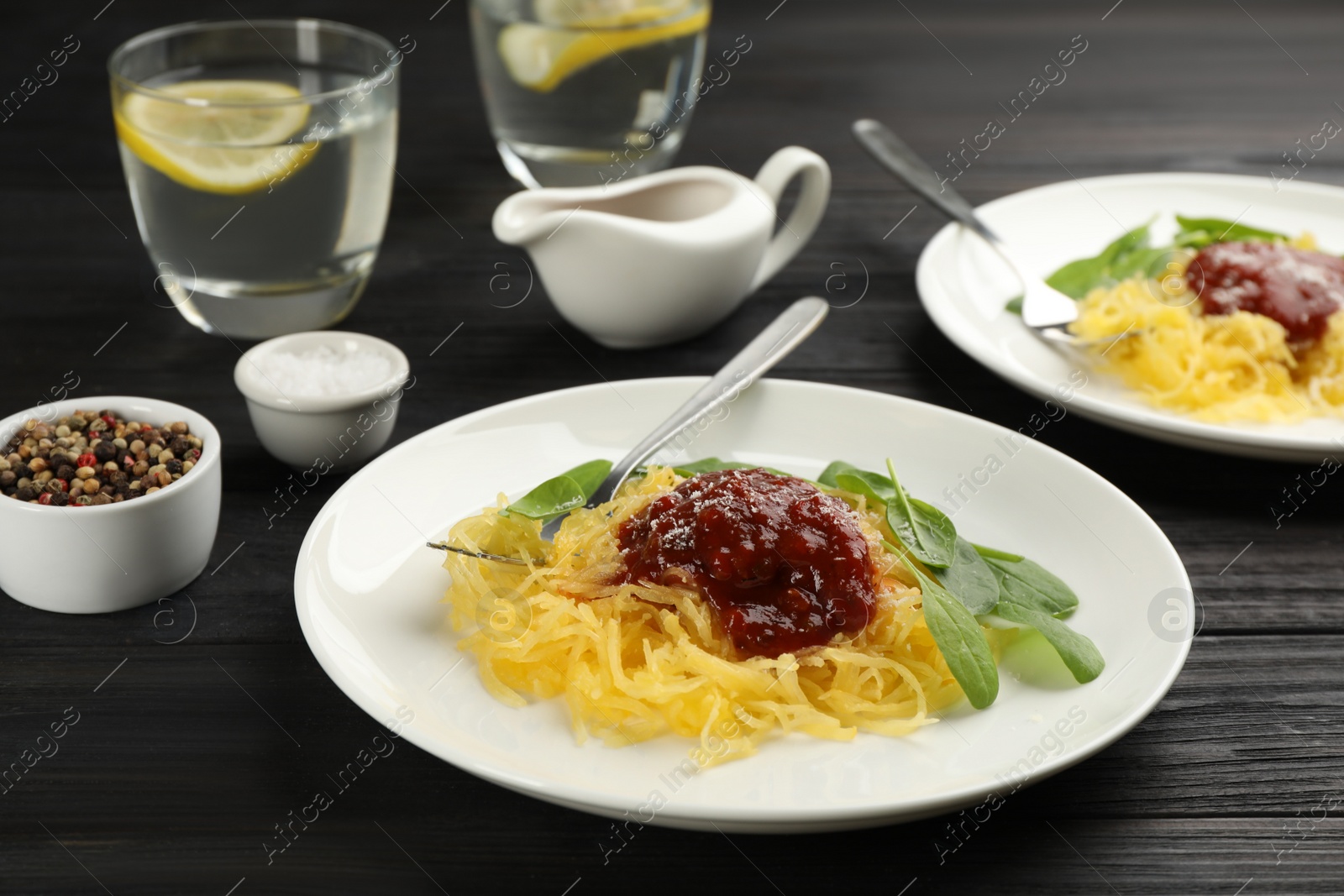 Photo of Tasty spaghetti squash with tomato sauce, cheese  and basil served on black wooden table