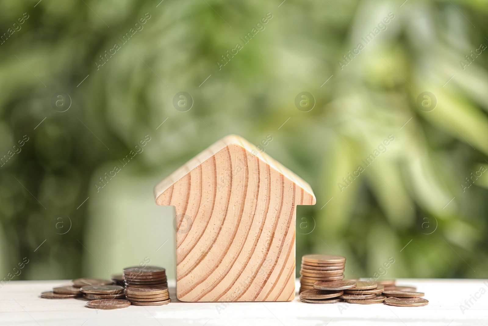 Photo of House model and coins on white table against blurred green background