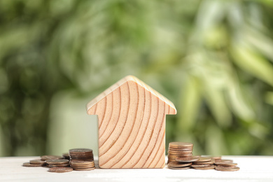 House model and coins on white table against blurred green background