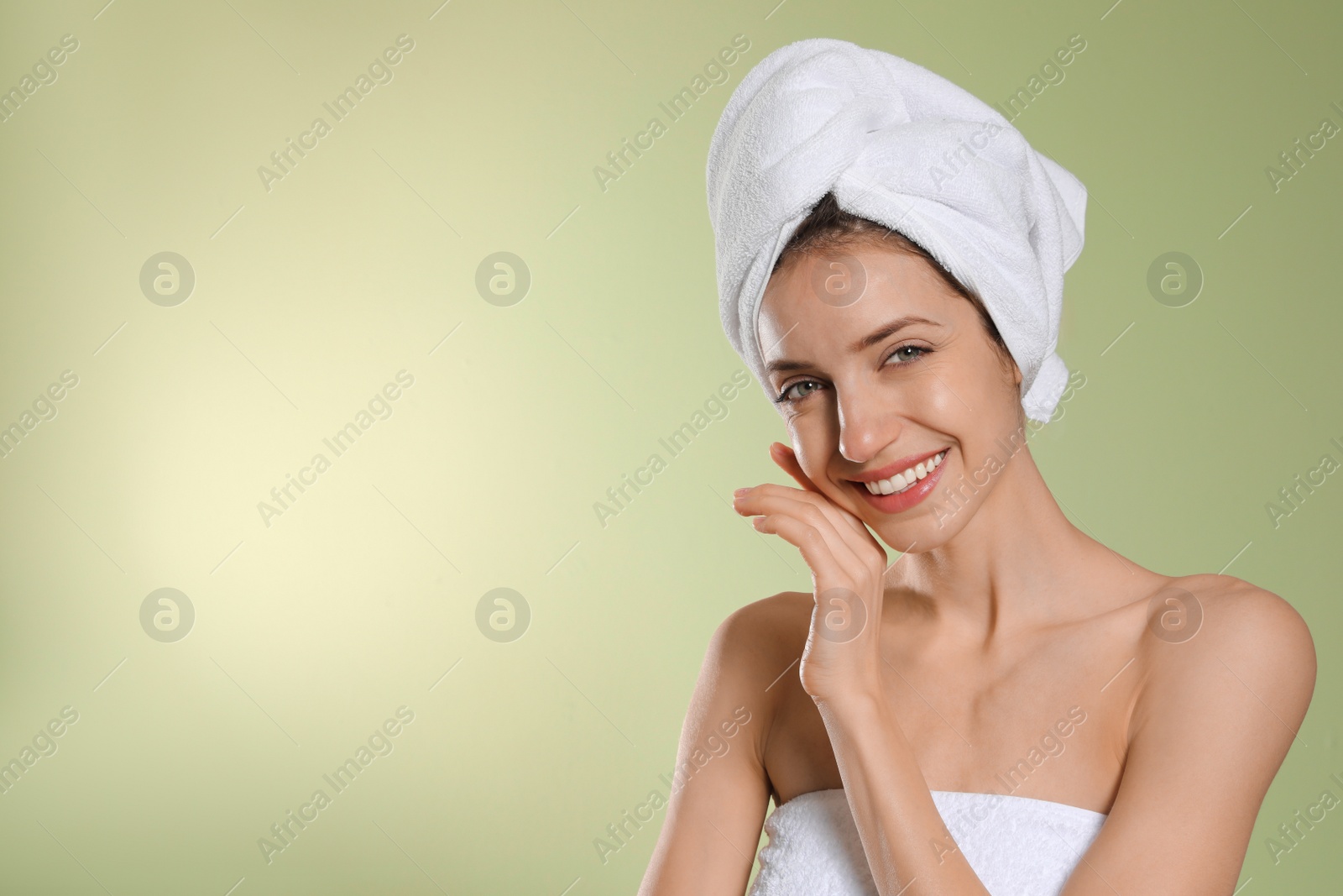 Photo of Beautiful young woman with hair wrapped in towel after washing on light green background. Space for text