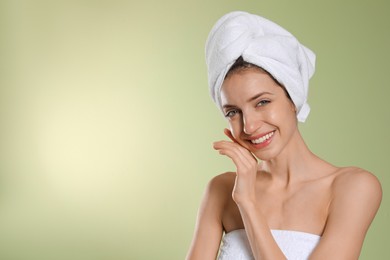 Beautiful young woman with hair wrapped in towel after washing on light green background. Space for text