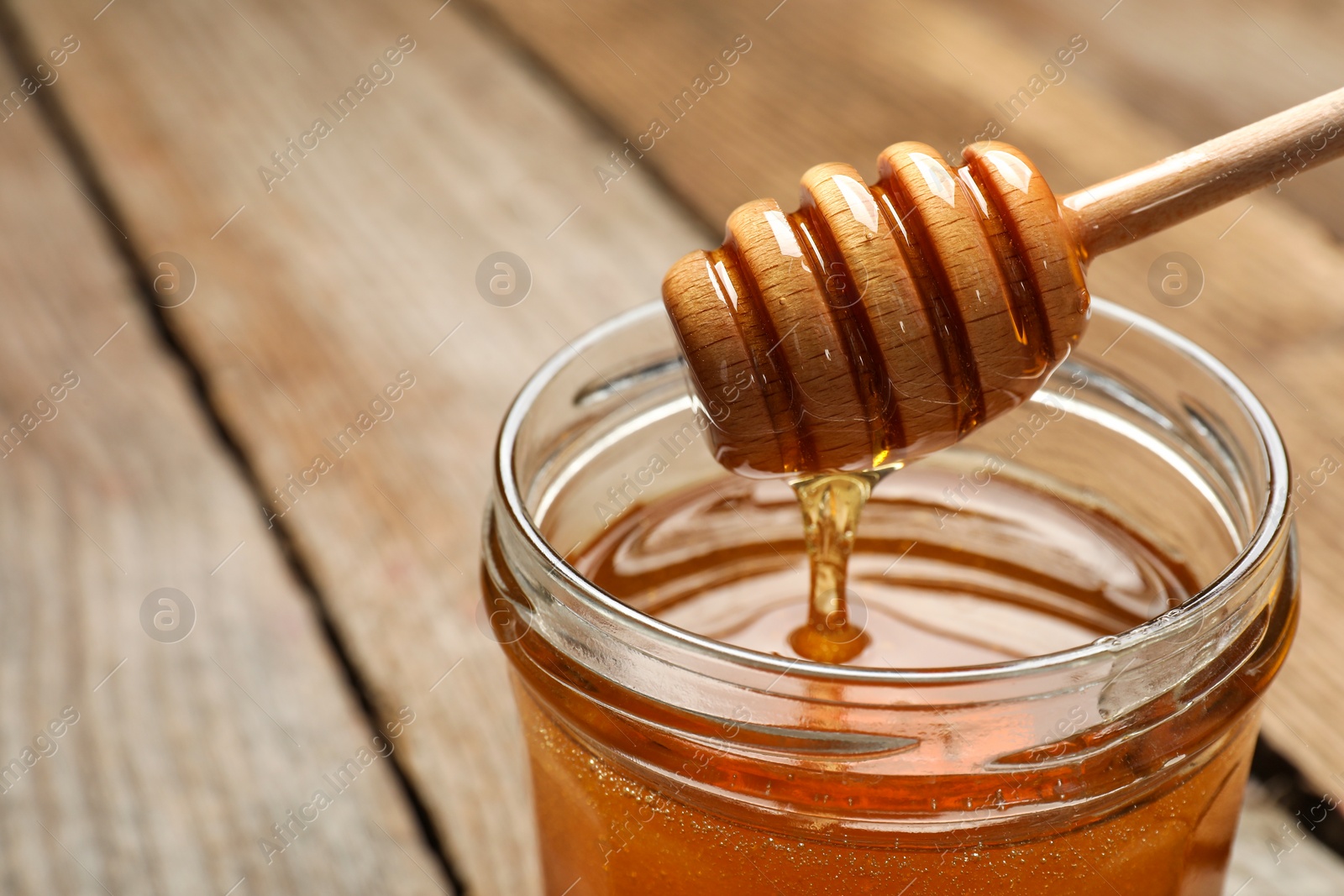 Photo of Pouring honey from dipper into jar on table, closeup. Space for text