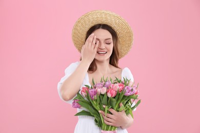 Photo of Happy young woman in straw hat holding bouquet of beautiful tulips on pink background