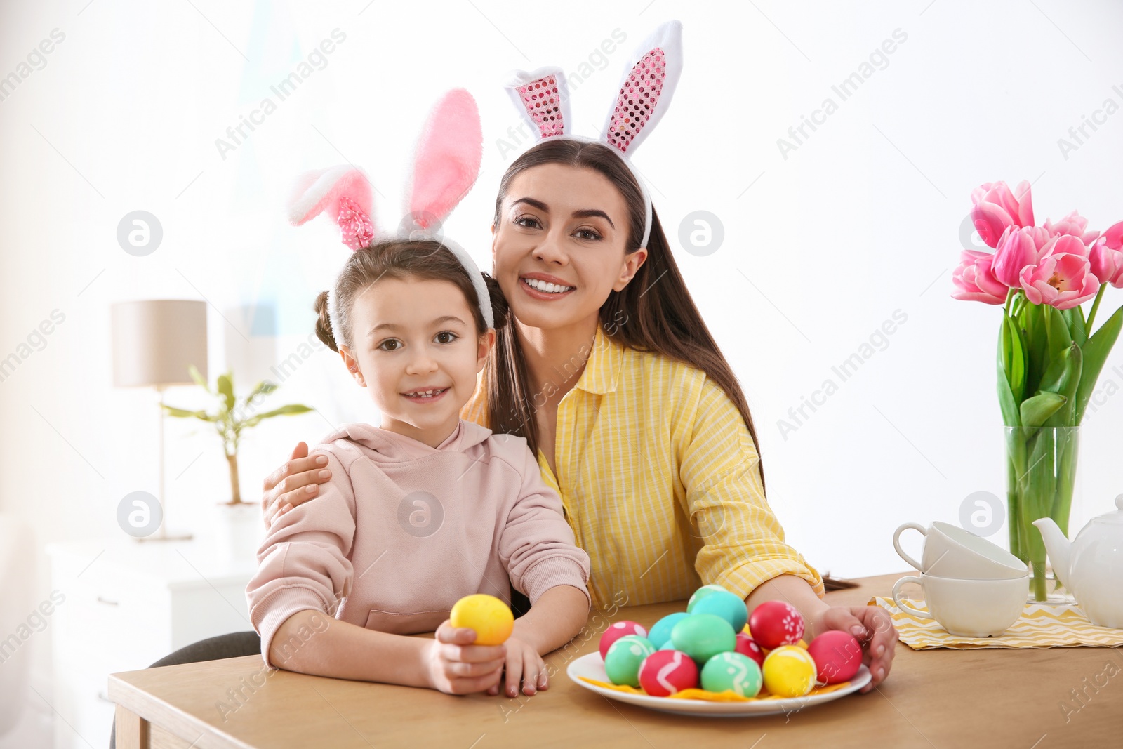 Photo of Mother and daughter with bunny ears headbands and painted Easter eggs at home