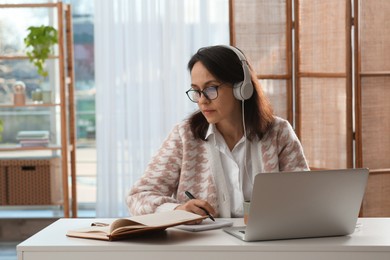 Photo of Woman with modern laptop and headphones learning at home