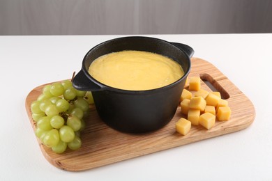 Photo of Fondue with tasty melted cheese and grapes on white table