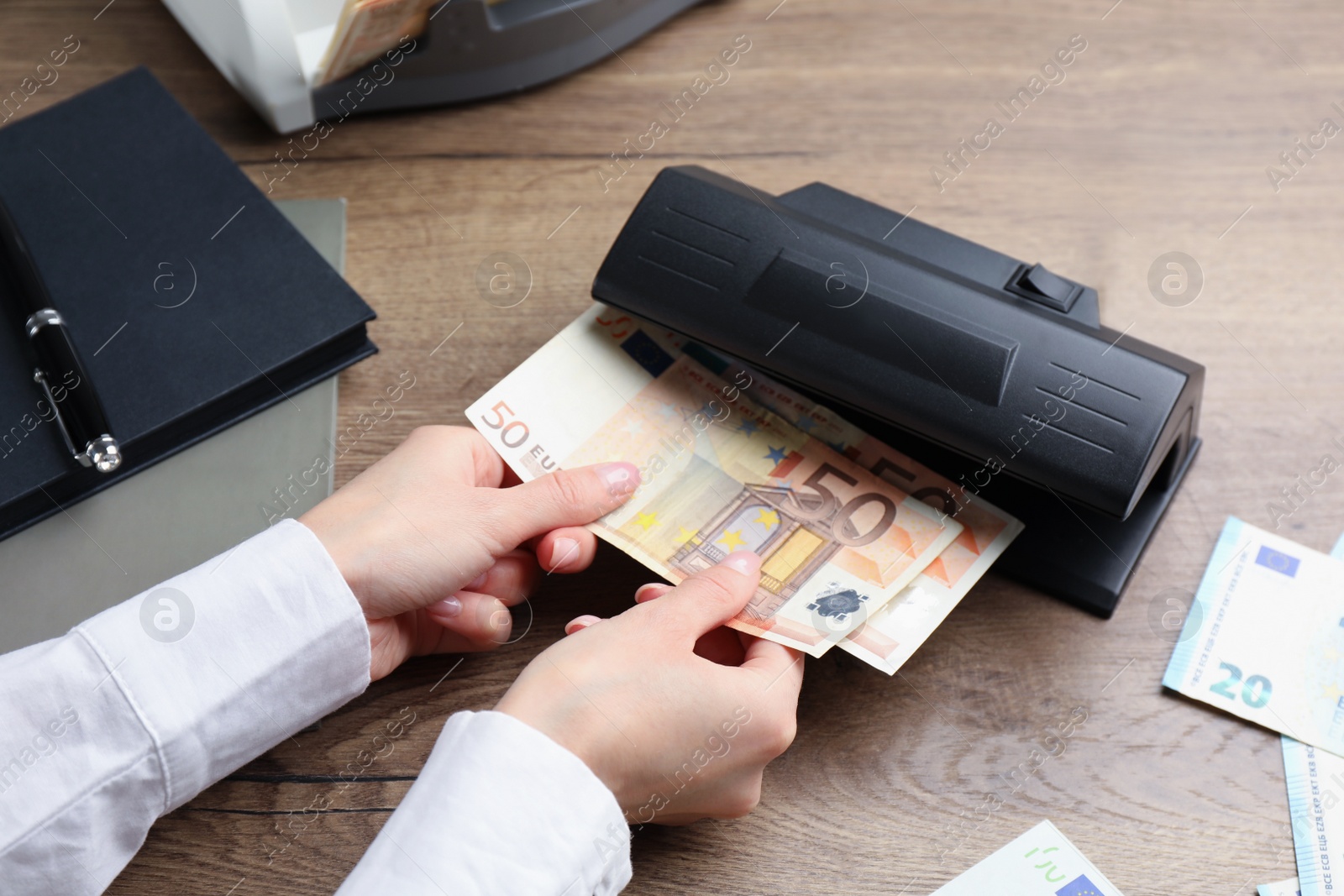 Photo of Woman checking Euro banknotes with currency detector at wooden table, closeup. Money examination device