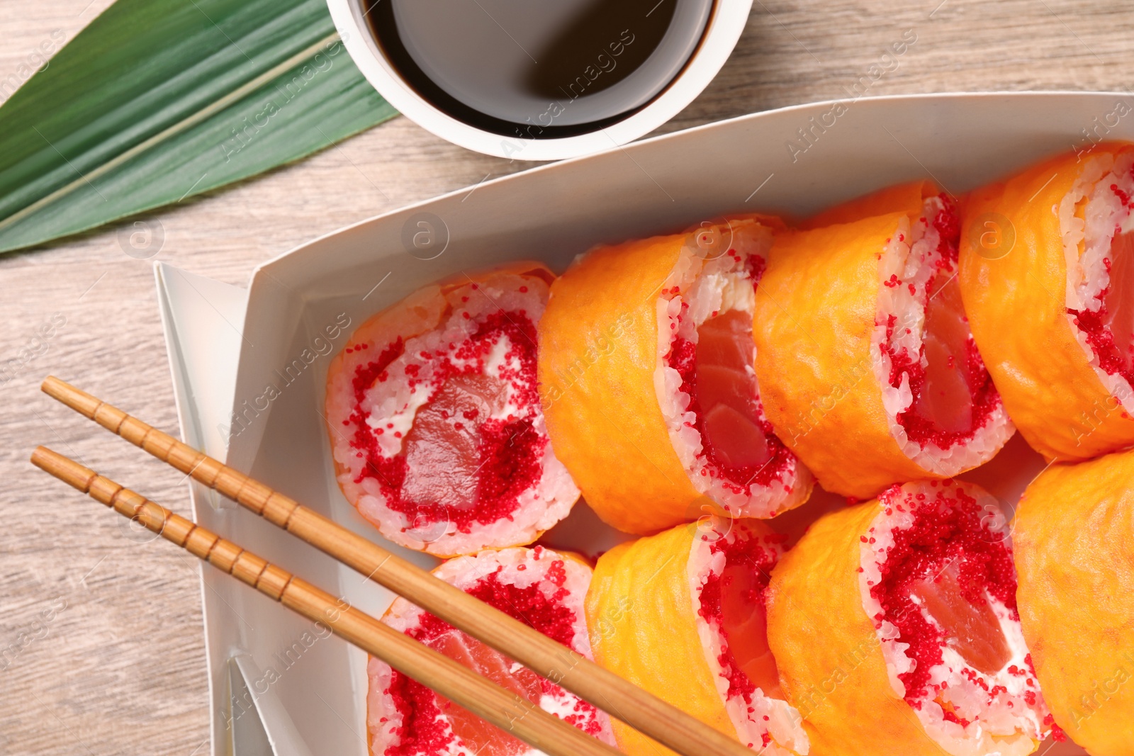 Photo of Food delivery. Delicious sushi rolls, chopsticks and soy sauce on wooden table, closeup