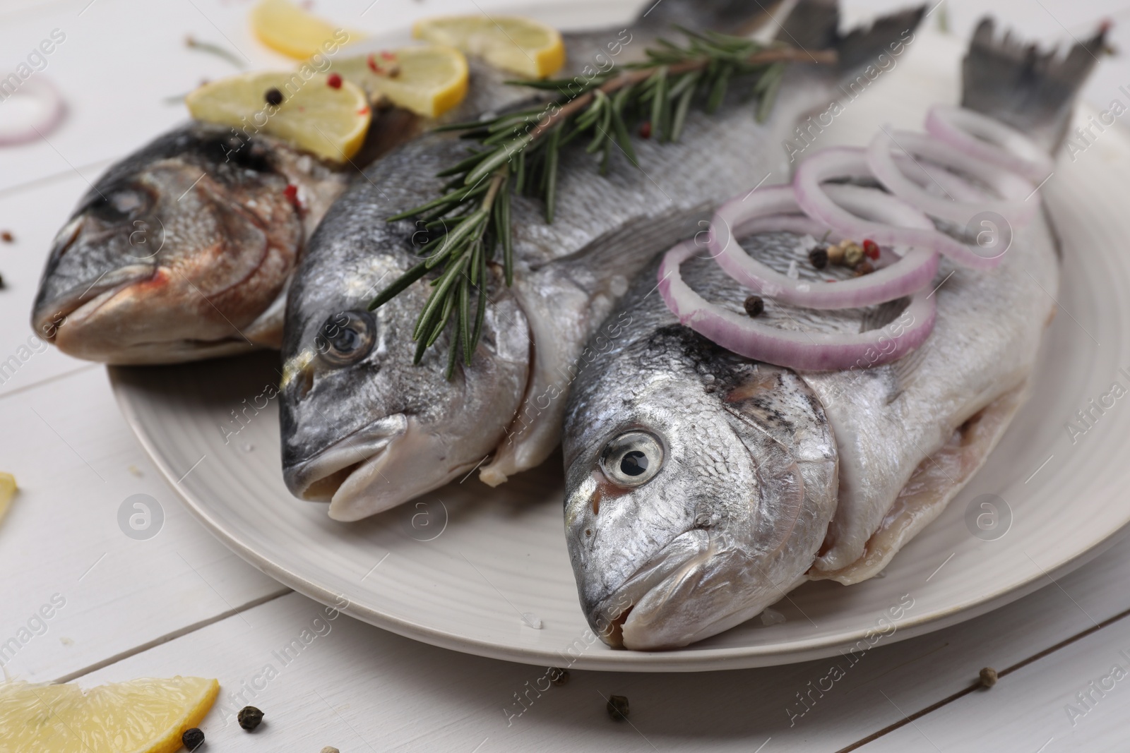 Photo of Raw dorado fish with lemon, rosemary and onion on white wooden table, closeup