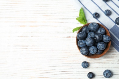 Photo of Bowl of tasty blueberries, leaves and fabric on white wooden table, flat lay with space for text