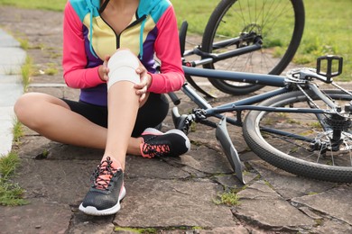 Photo of Young woman with injured knee near bicycle outdoors, closeup