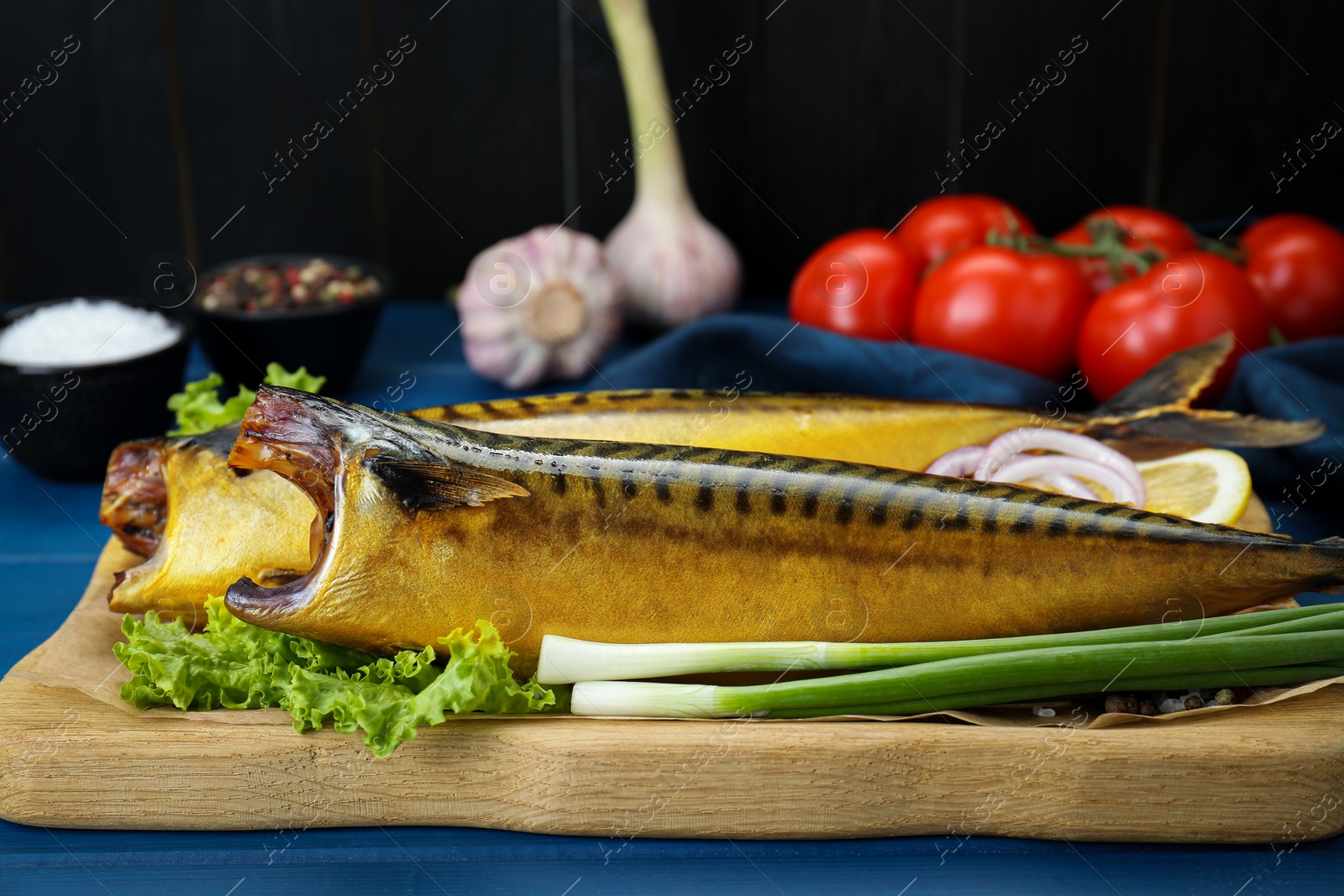 Photo of Delicious smoked mackerels, green onions and lettuce on blue table, closeup