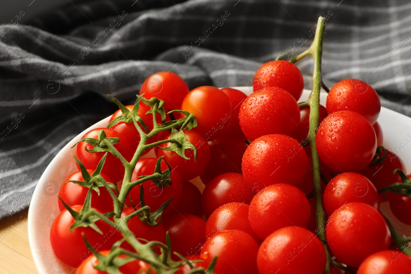 Photo of Plate of ripe whole cherry tomatoes with water drops on table, closeup