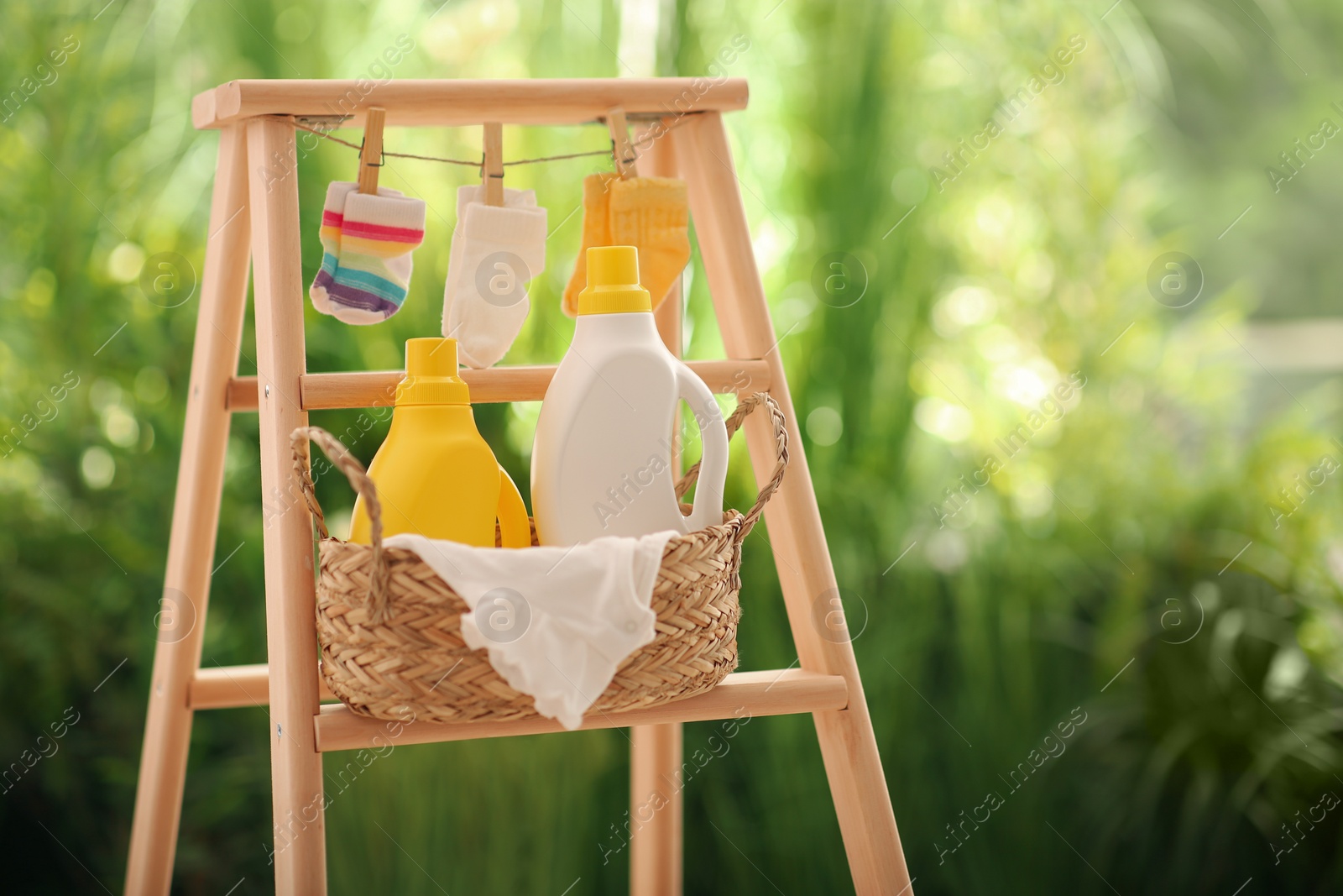 Photo of Bottles of detergent and children's clothes on wooden ladder outdoors